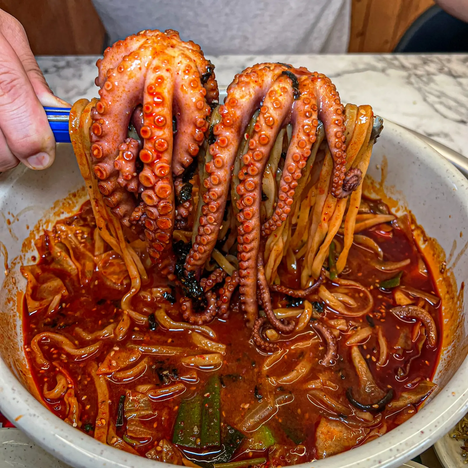 집게로 들어 올린 낙지와 양념 면이 담긴 오봉집 낙지 면 요리